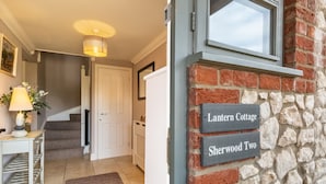 Eine Treppe führt zu einer Tür, einer Lampe, einem Tisch mit einer Vase und einer Wand mit Schildern mit den Aufschriften 'Lantern Cottage' und 'Sherwood Two'.