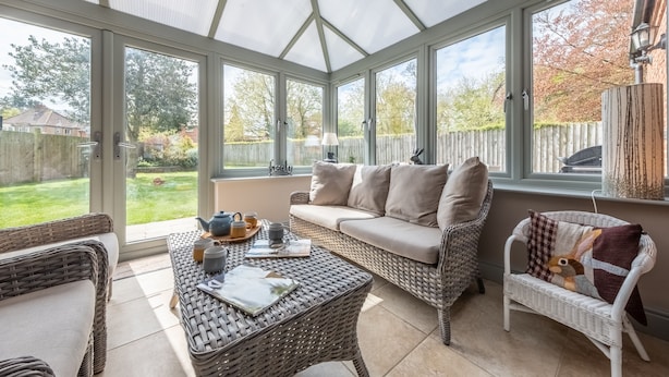 Ein Wintergarten mit Korbmöbeln, einer Couch und einem Tisch mit Teeservice.