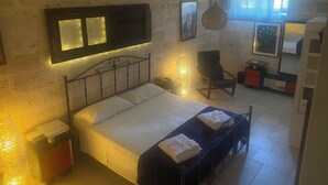 Un dormitorio con cama, mesitas de noche, una silla y una pequeña mesa con lámpara.