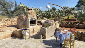 Un área de comedor al aire libre con un horno de piedra, una mesa con mantel a cuadros y sillas.
