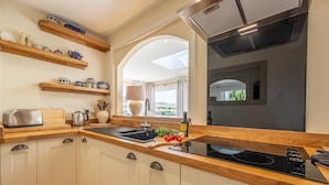A modern kitchen with white cabinets, wooden countertops, a built-in stove, and a window overlooking a garden. - Tanholt, Holme-next-the-Sea, Norfolk (Holme-next-the-Sea)