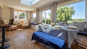 A dining area with a table set for four, large windows, and a view of greenery. - Tanholt, Holme-next-the-Sea, Norfolk (Holme-next-the-Sea)