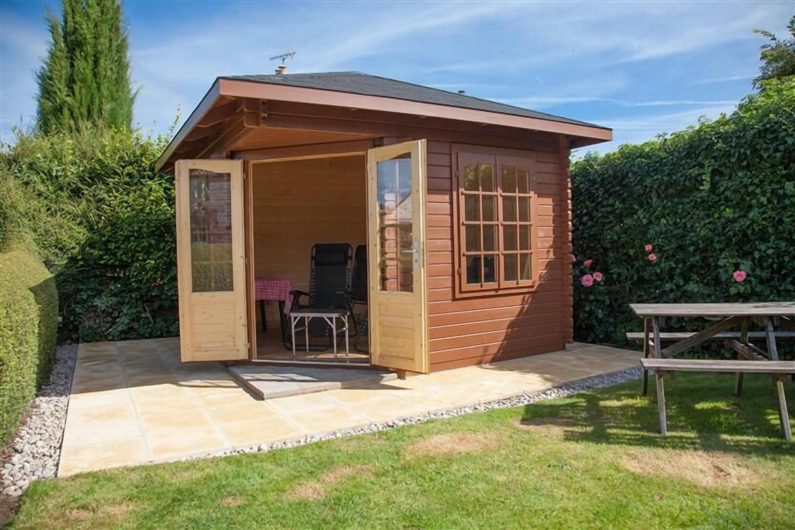 Une cabane en bois avec une porte ouverte, un espace patio et une table de pique-nique.