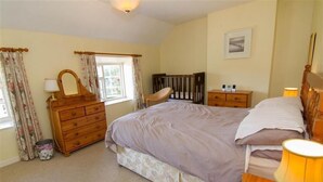 Een slaapkamer met een bed, een houten dressoir, nachtkastje en een raam met gordijnen.