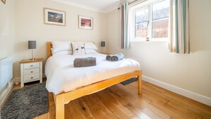 Un dormitorio con una cama de madera, ropa de cama blanca, una mesita de noche, dos lámparas de pared y una ventana con cortinas.