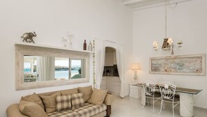 Un salon confortable avec un canapé, une table à manger et des chaises, une cuisine en arrière-plan et une grande fenêtre donnant sur la mer.