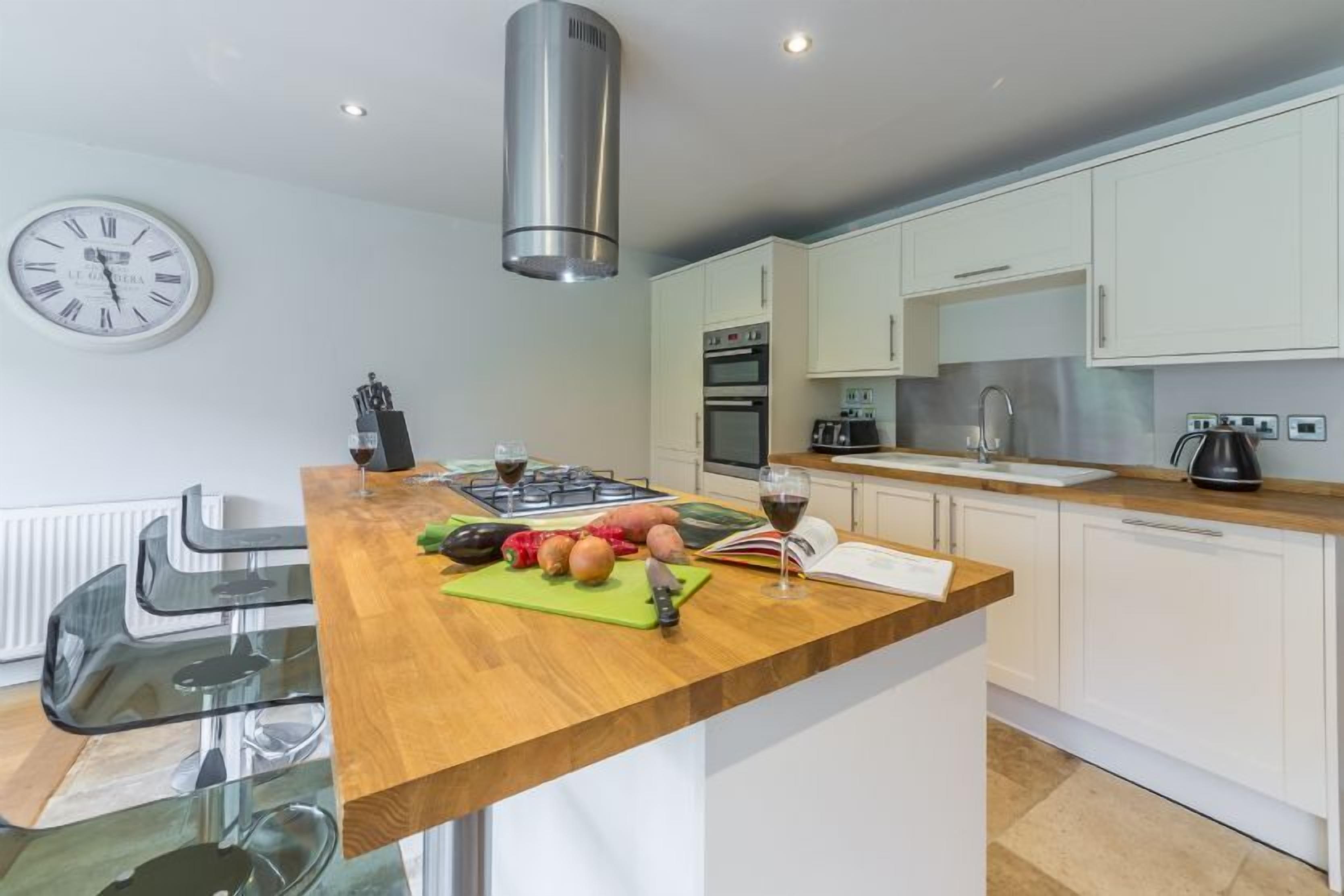 Une cuisine moderne avec un îlot central en bois, des appareils électroménagers en acier inoxydable et une horloge au mur.