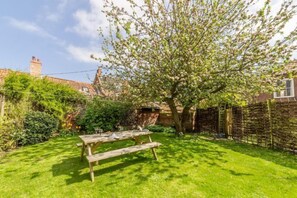 A backyard with a wooden picnic table, a tree, and a brick wall. - Holly House, Wells-next-the-Sea, Norfolk (Wells-Next-The-Sea)