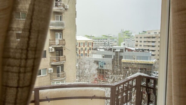A view from a balcony with a railing, overlooking a residential area with multiple buildings and a clear sky. - Motru 84 by MRG Apartments | Central | Balcony | Metro | Park & Amenities (București)