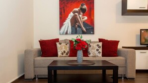A living room with a sofa, red pillows, a vase with flowers, and a painting on the wall. - Motru 84 by MRG Apartments | Central | Balcony | Metro | Park & Amenities (București)