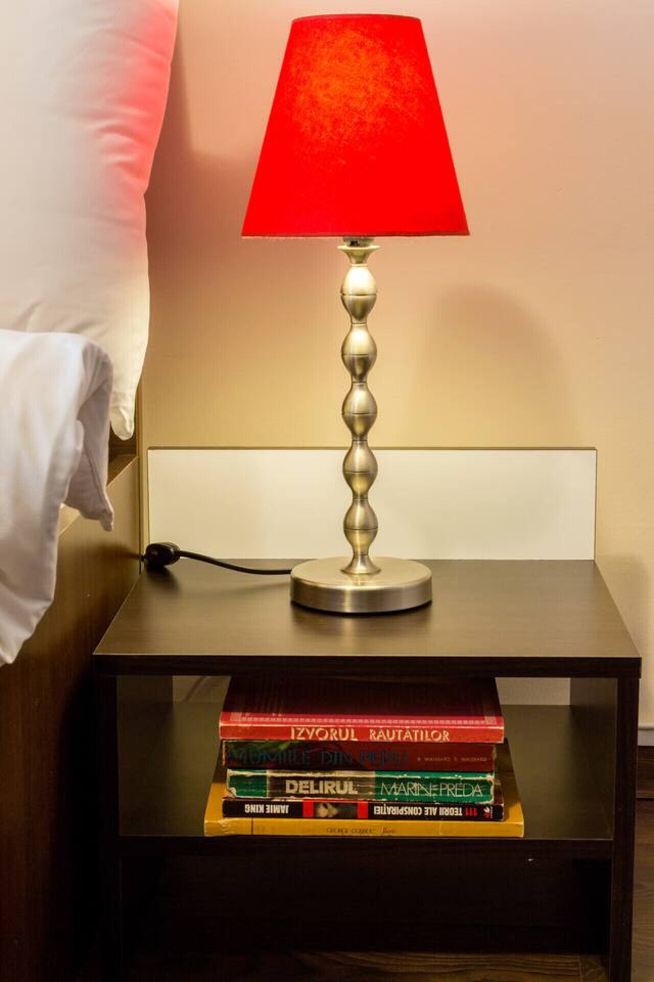 Uma mesa de cabeceira com uma luminária, uma pilha de livros e uma almofada.