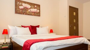A neatly made bed with white and red bedding, two bedside lamps, and a door in the background. - Motru 84 by MRG Apartments | Central | Balcony | Metro | Park & Amenities (București)