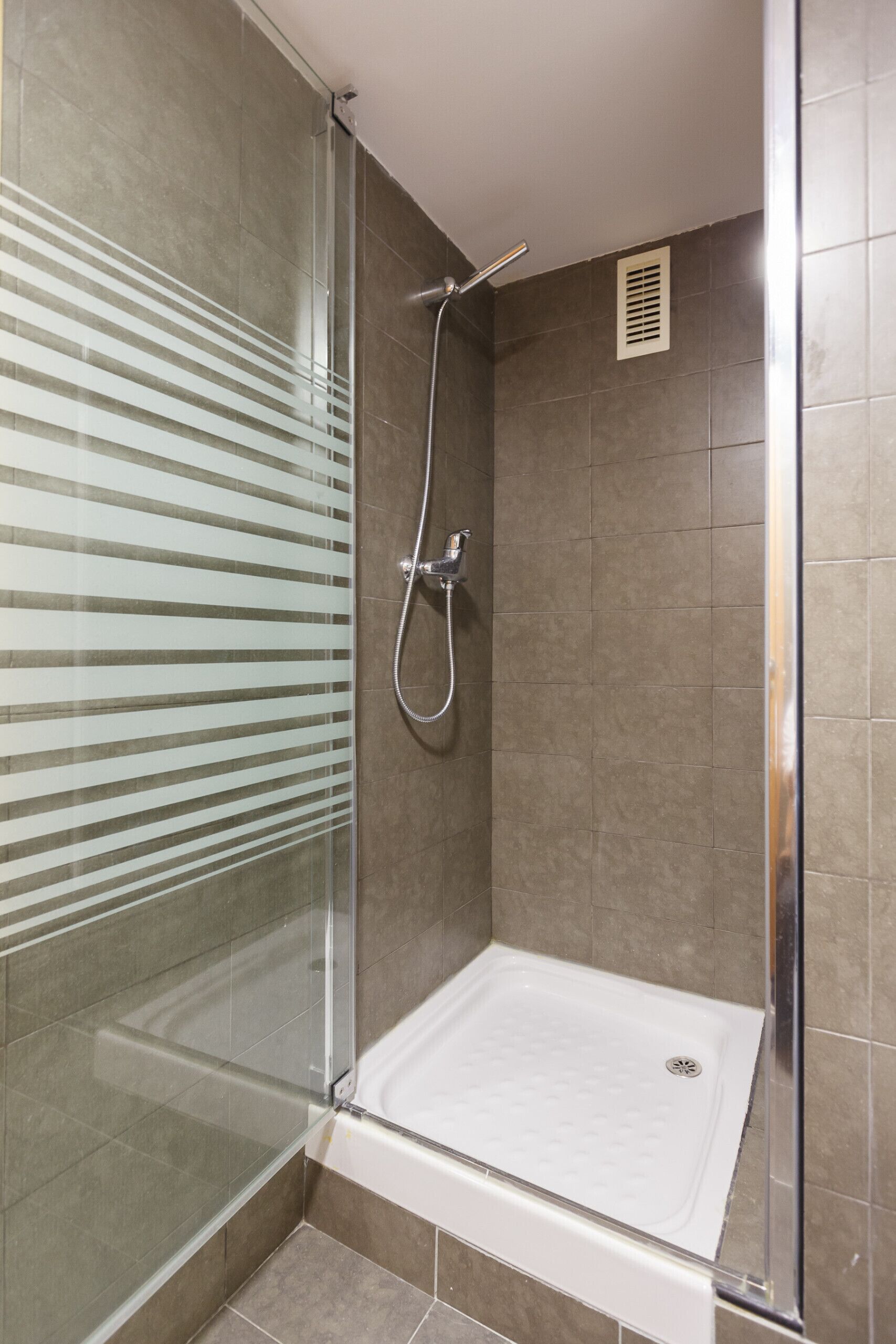 A shower with a glass door, a handheld showerhead, and a white bathtub.