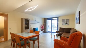 A modern living room with a dining area, a sofa, and a TV. - Apartment in Family Complex 50m beach · UHC MAR AUGUSTA 212 (Cambrils)