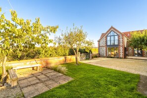 A brick house with a large glass window, a grassy yard, and a wooden bench. - Plumtrees, Thornham, Norfolk (Thornham)