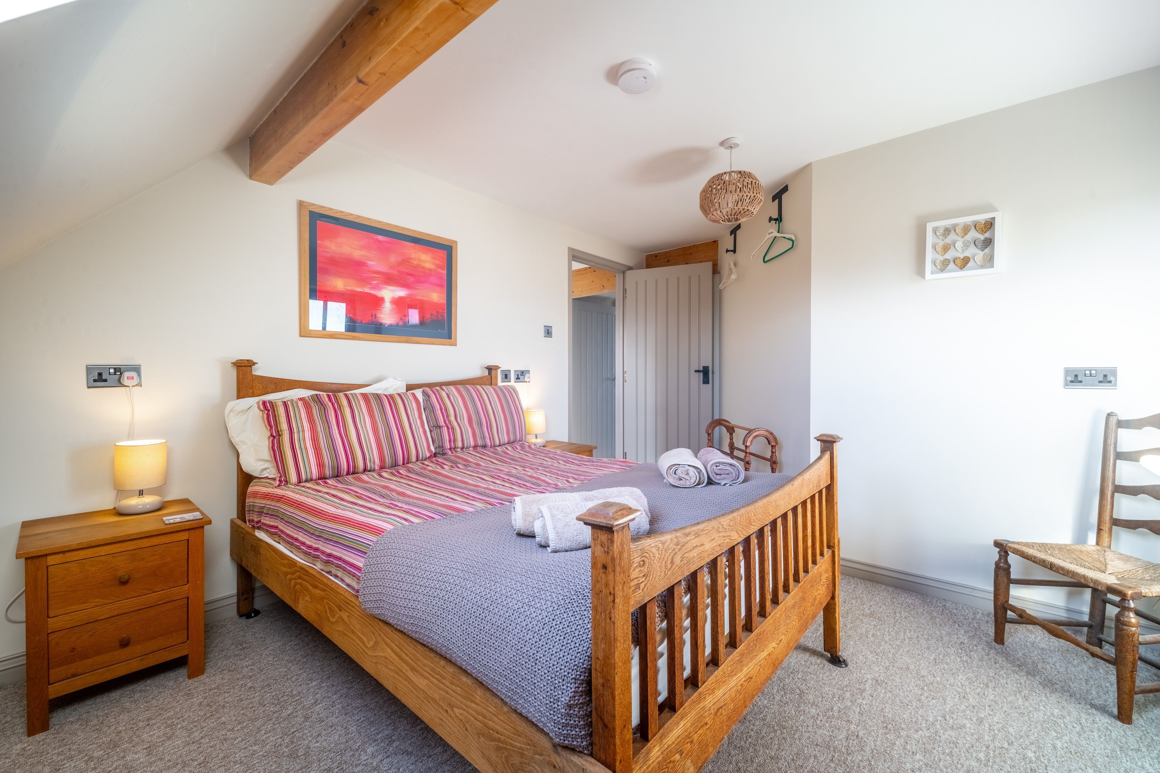 Une chambre à coucher avec un lit en bois, une table de chevet, une lampe, une chaise et une porte donnant sur une autre pièce.
