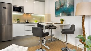 A modern kitchen with white cabinets, a stainless steel refrigerator, a microwave, and a dining area with a table and two bar stools. - Genteel Home Baños Terrace (Seville)