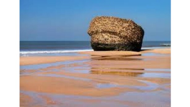 Una gran formación rocosa en una playa con el océano al fondo.