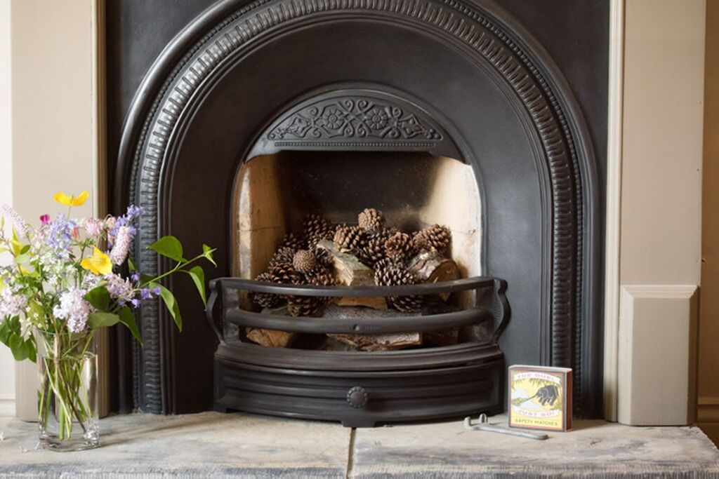 A fireplace with a decorative surround, a vase with flowers, and a book on the mantel.