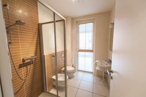 Un baño con cabina de ducha de vidrio, inodoro y lavamanos.