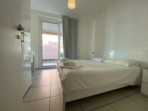 A hotel room with a bed, a nightstand, a door, and a view of the outside. - Modern Italian Lakes apartment with pool (Maccagno con Pino e Veddasca)
