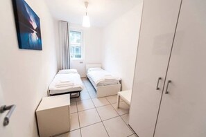 Una habitación pequeña y limpia con dos camas, un armario y una ventana.