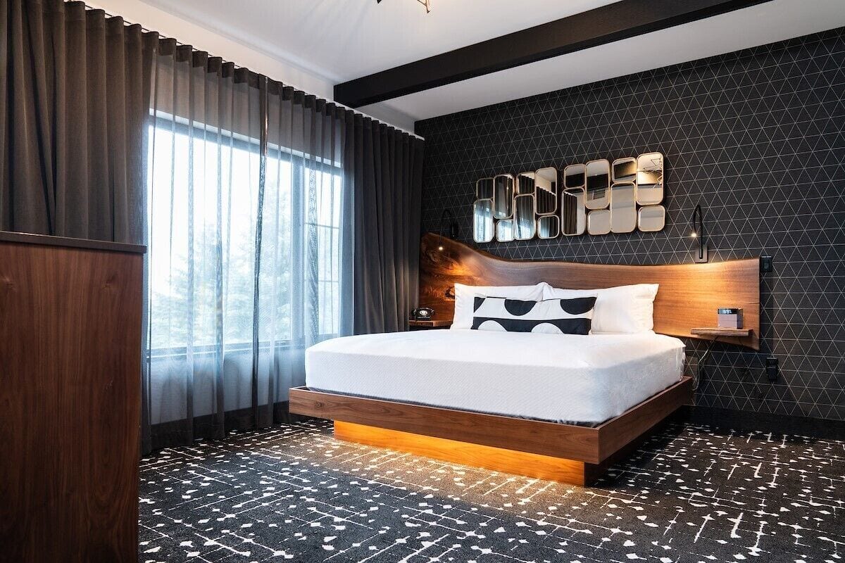 A modern bedroom with a wooden bed frame, a geometric wall design, and a large window with curtains.