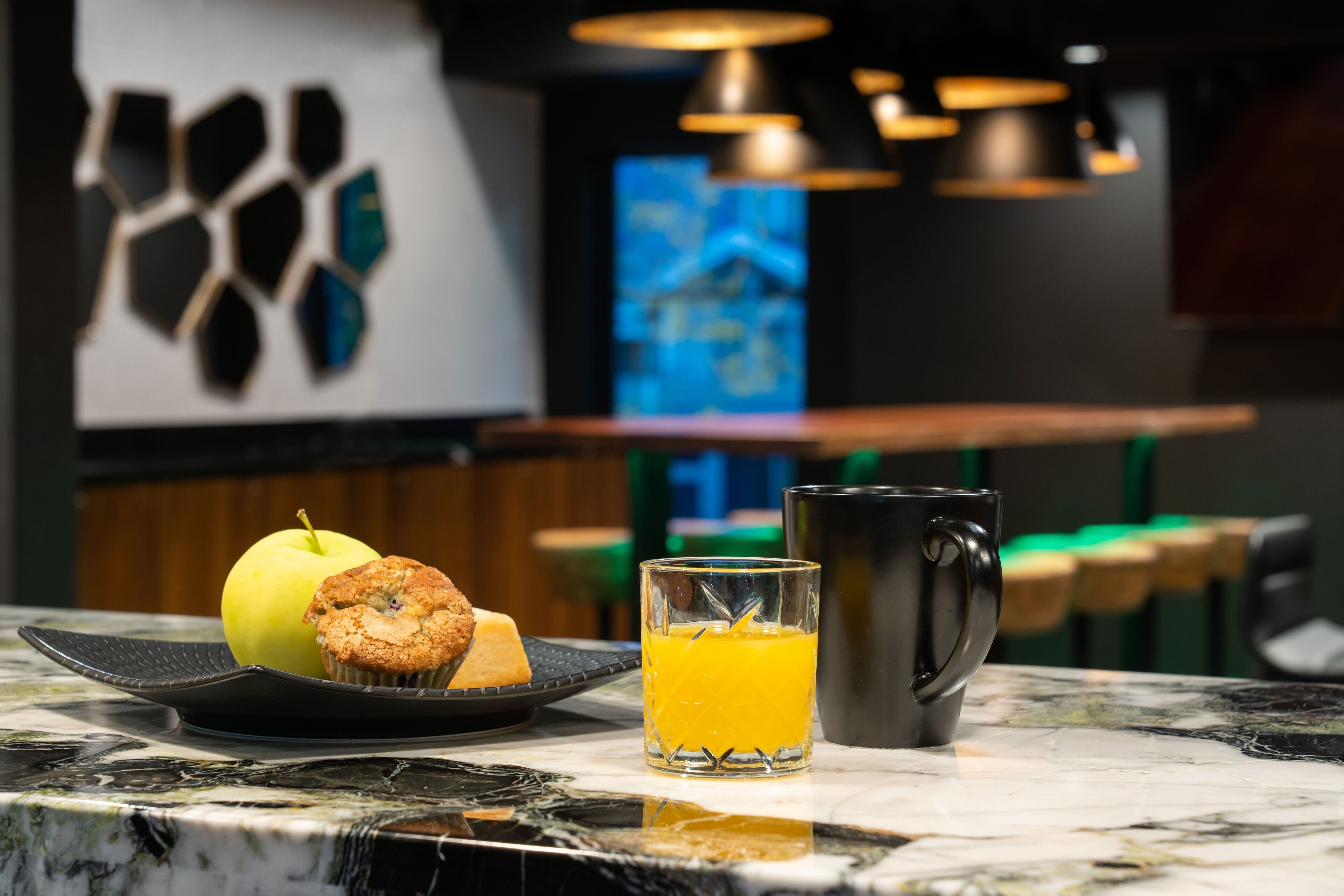 A breakfast setting with a plate of food, a glass of orange juice, and a mug on a marble countertop.