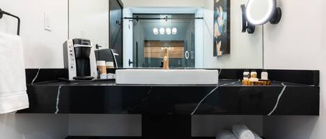 A modern bathroom with a black marble countertop, a coffee machine, a sink, and a towel rack.