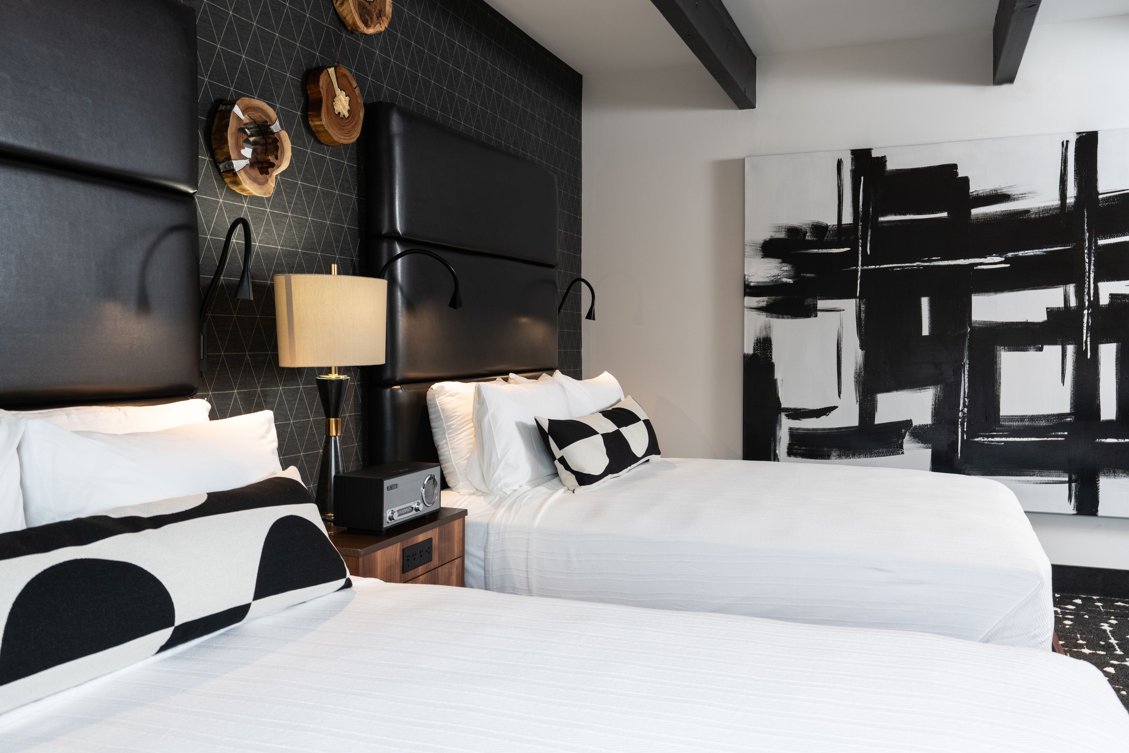 A modern hotel room with two beds, a large abstract painting, and a unique black and white patterned wall.