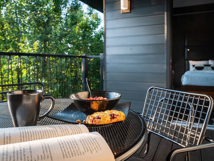 Un balcón con una silla de metal, una taza de metal, un tazón de comida y un libro abierto.