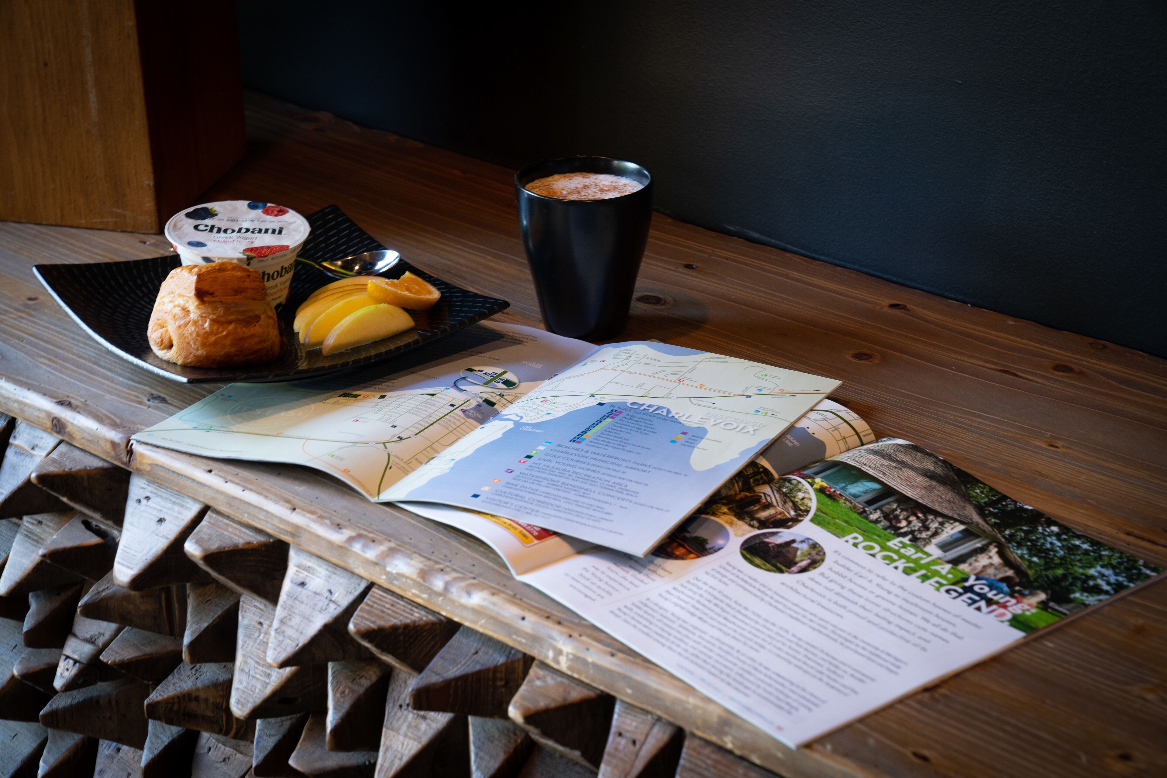 Una mesa de madera con un plato de comida, una taza y un folleto abierto.