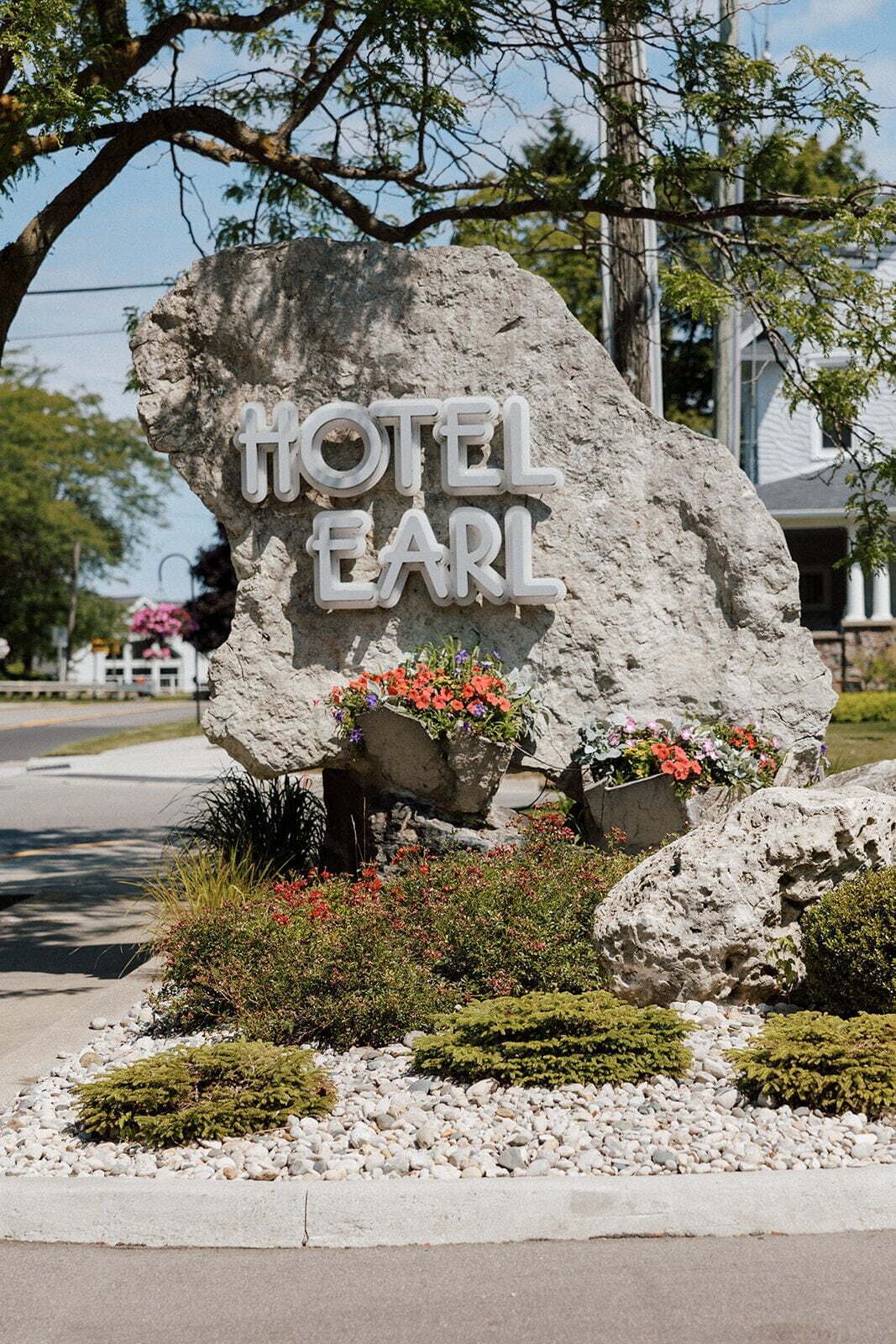 A large rock with "HOTEL EARL" engraved on it, surrounded by potted plants and shrubs.