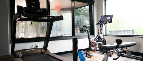 Un gimnasio con cinta de correr, bicicleta estática y banco de pesas.