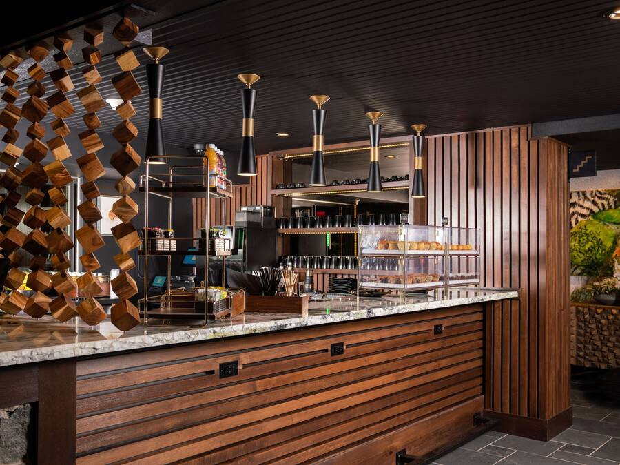 Zona de bar moderna amb panells de fusta, taulell de marbre i il·luminàries penjants.