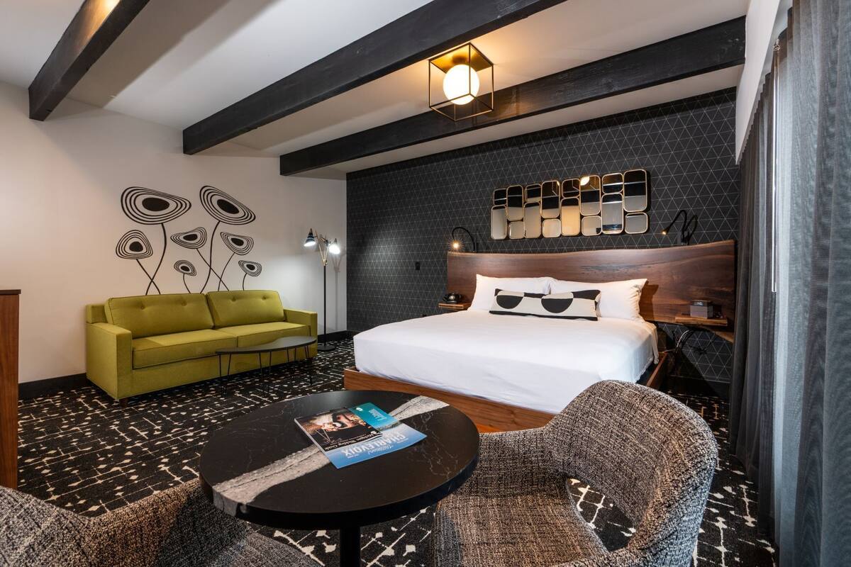A hotel room with a bed, a green sofa, a round coffee table, and a patterned carpet.