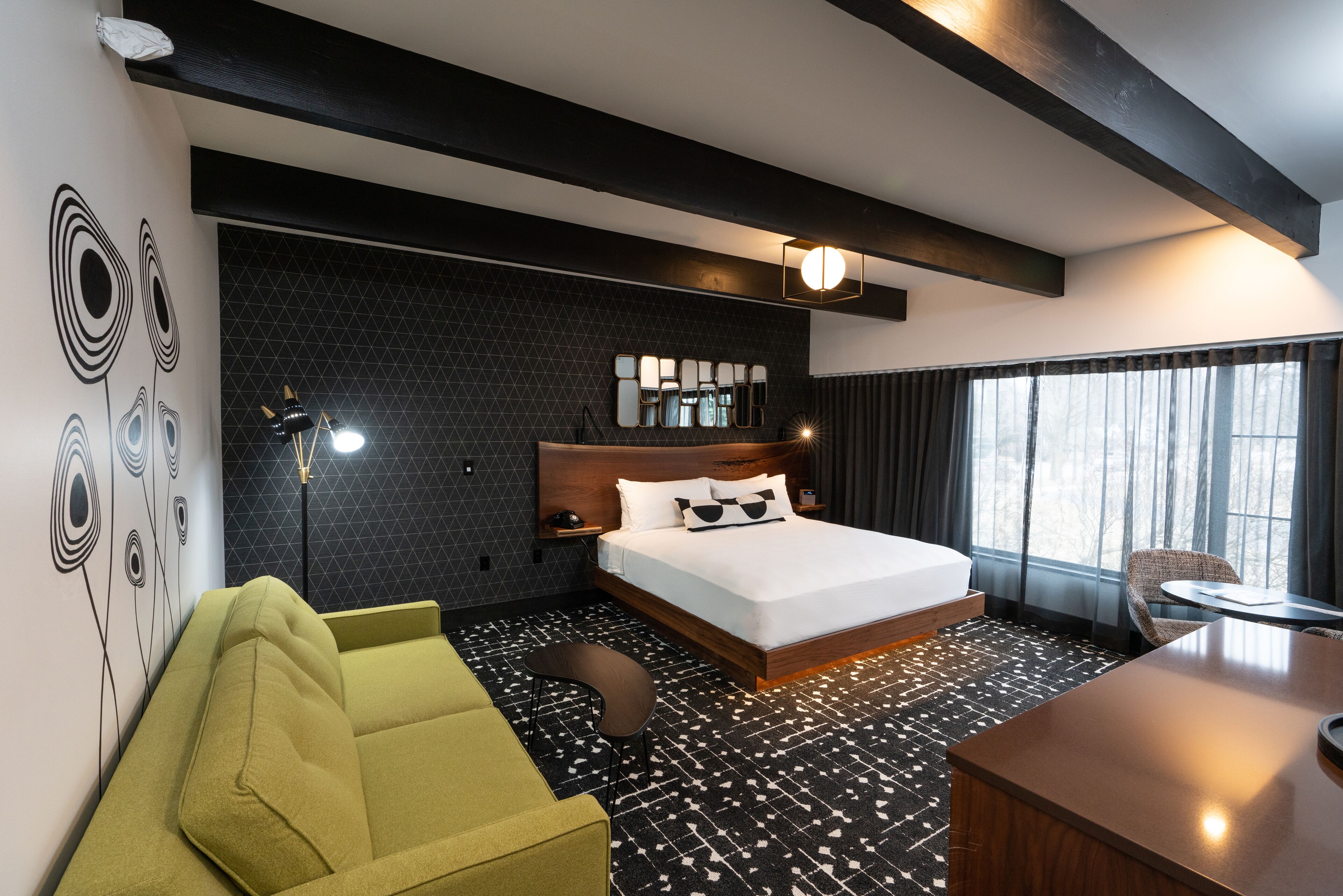 A modern hotel room with a large bed, a desk, and a green armchair.