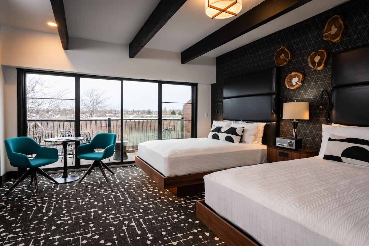 A hotel room with two beds, a large window, a small table with chairs, and a modern ceiling design.