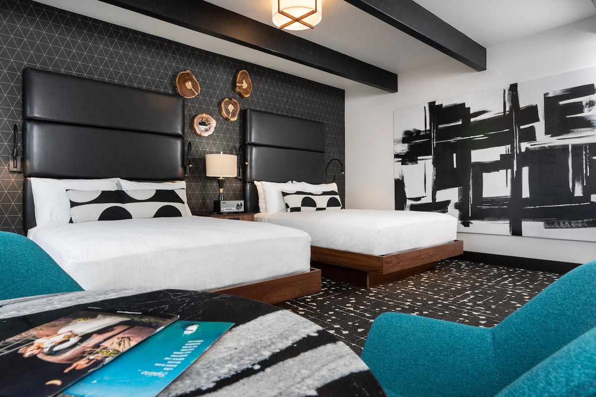 A modern hotel room with two beds, a large abstract painting, and a unique geometric floor pattern.