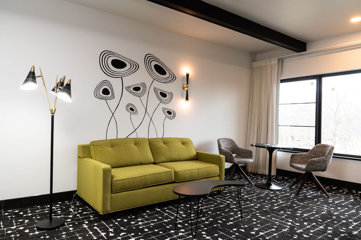 A modern living room with a green sofa, two armchairs, a small table, a floor lamp, and a wall art piece.