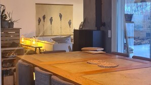 A spacious dining area with a long wooden table and six chairs, a modern pendant light, and a view of the outdoors through a large window. - Peaceful designed modern villa nestles in St Paul de Vence (saint paul de vence)