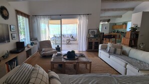 A spacious living room with a sofa, a coffee table, and a TV. There is a sliding glass door leading to an outdoor area with a table and chairs. - Peaceful designed modern villa nestles in St Paul de Vence (saint paul de vence)