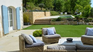 A patio with wicker furniture, a stone wall, and a view of a pool and garden. - Peaceful designed modern villa nestles in St Paul de Vence (saint paul de vence)