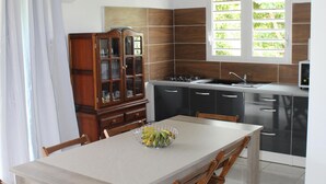 A modern kitchen with a dining area, featuring a large island, wooden chairs, and a cabinet with glass doors.