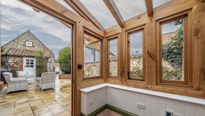 A conservatory with wooden beams, large windows, and a white bench. - Mill House Cottage, Brancaster, Norfolk (King's Lynn)