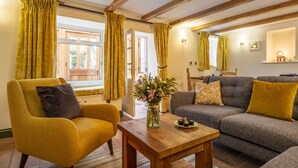 A cozy living room with a yellow armchair, a grey sofa, and a wooden coffee table with a vase of flowers. - Mill House Cottage, Brancaster, Norfolk (King's Lynn)