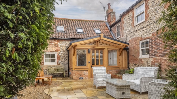 A patio area with wicker furniture, a wooden door, and a stone-tiled floor. - Mill House Cottage, Brancaster, Norfolk (King's Lynn)