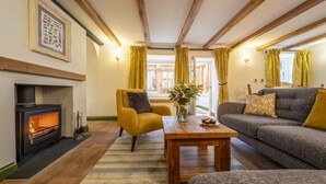 A cozy living room with a fireplace, a sofa, a coffee table, and a yellow armchair. - Mill House Cottage, Brancaster, Norfolk (King's Lynn)