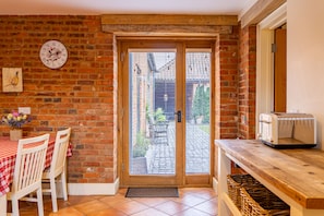 A room with a brick wall, a wooden door with a window, a table with chairs, and a toaster on a wooden counter. - The Dairy, Great Massingham, Norfolk (Great Massingham)