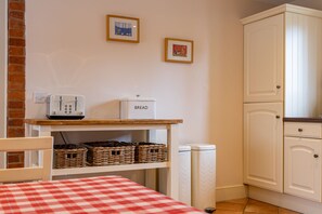 A kitchen with a toaster, bread box, wicker baskets, a recycling bin, and a white cabinet.